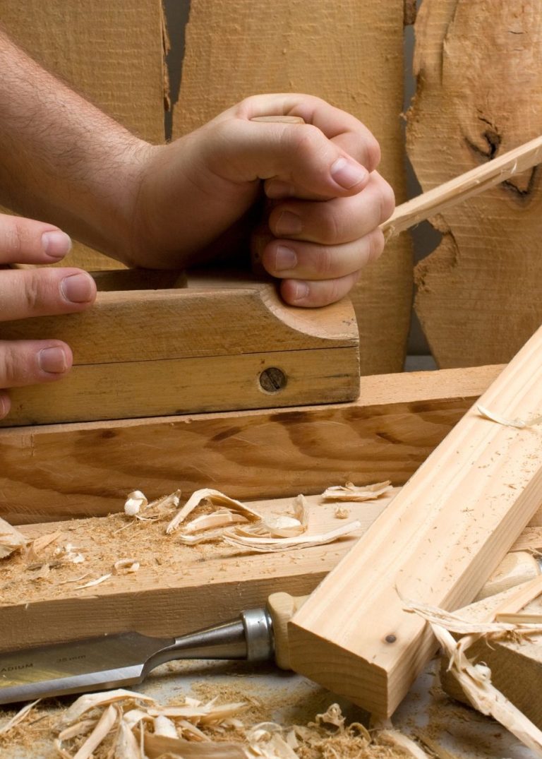 Hands using a hand plane on wood, surrounded by shavings.
